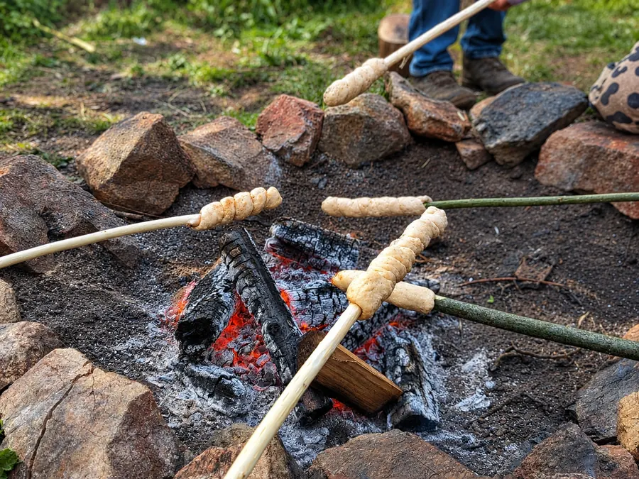 Twists of bread dough on sticks cooking over the embers of a stone fire circle