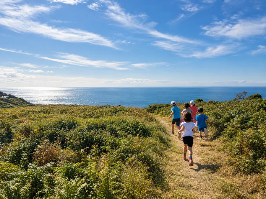 Children running along a clifftop path through bracken towards the sea