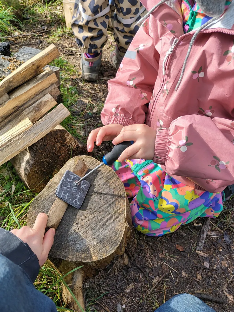 A child carefully carving letters into a piece of slate on a log